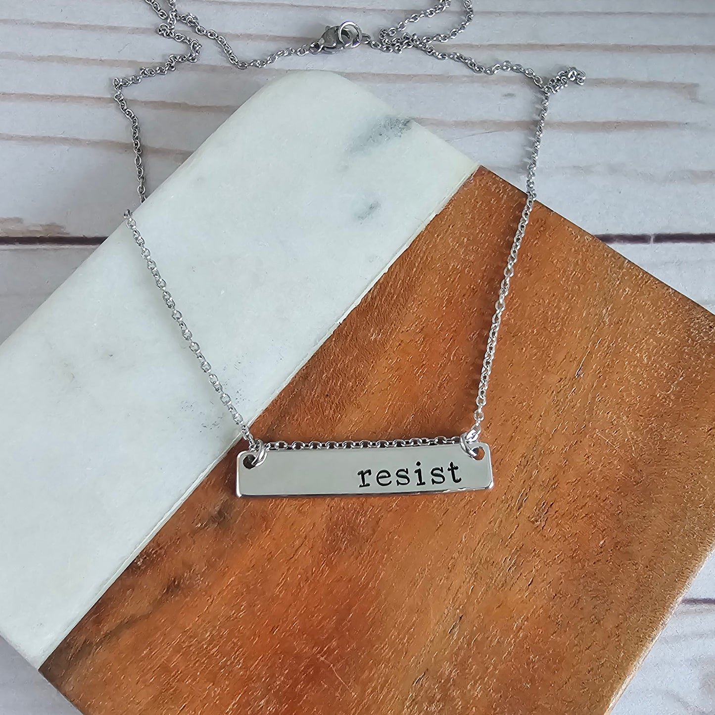 Silver horizontal bar that reads resist and is attached to a silver cable chain