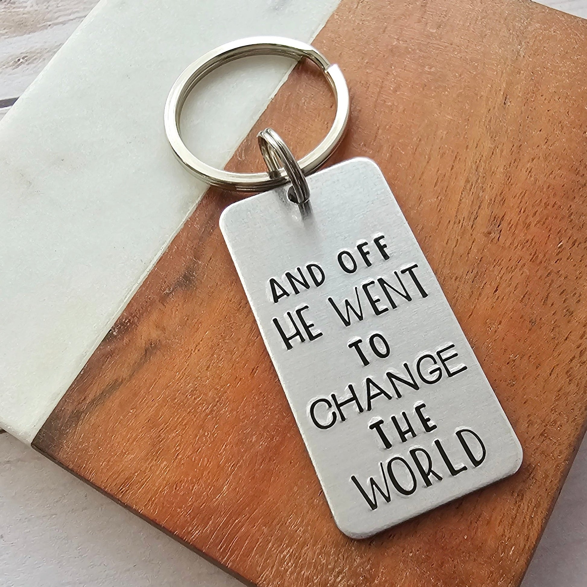 Silver rectangle tag that is hand stamped to read And off he went to change the world - the tag is attached to a split ring and key ring