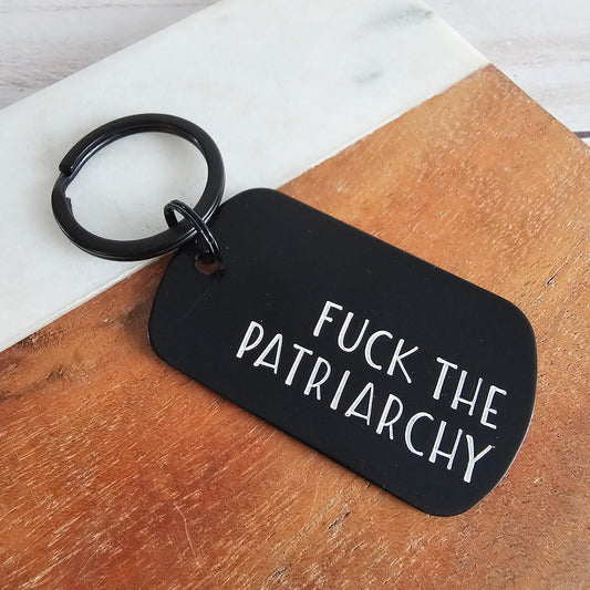 Black keychain with 'FUCK THE PATRIARCHY' text on a wooden surface