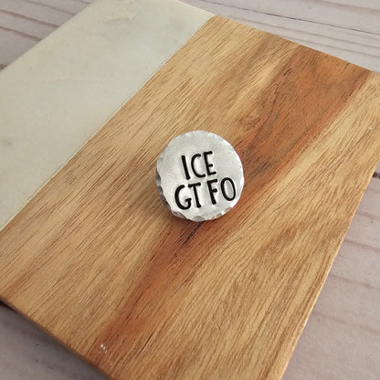 Round silver disc that reads ICE GTFO on a woodgrain background