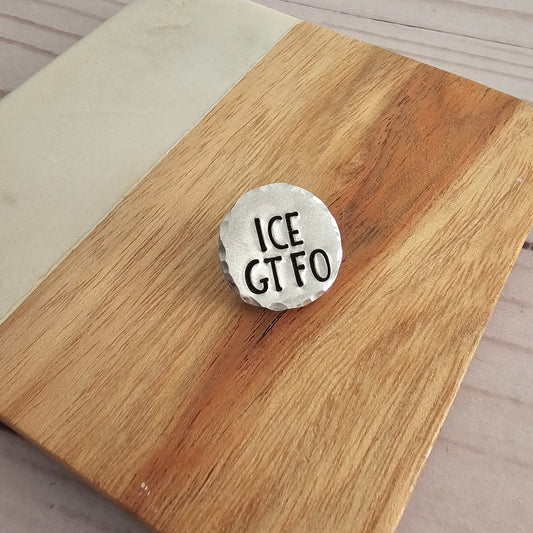 Round silver disc that reads ICE GTFO on a woodgrain background