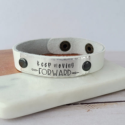 white leather cuff bracelet with metal plate that reads keep moving forward