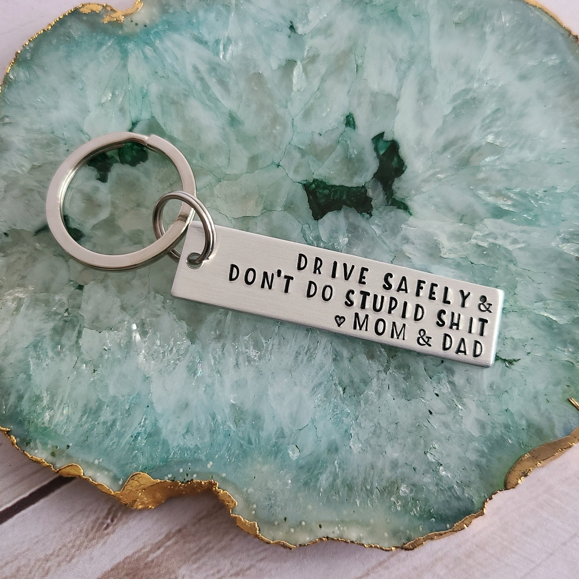 Silver metal keychain that is hand stamped to read Drive Safely & Don't Do Stupid Shit Love Mom and Dad
