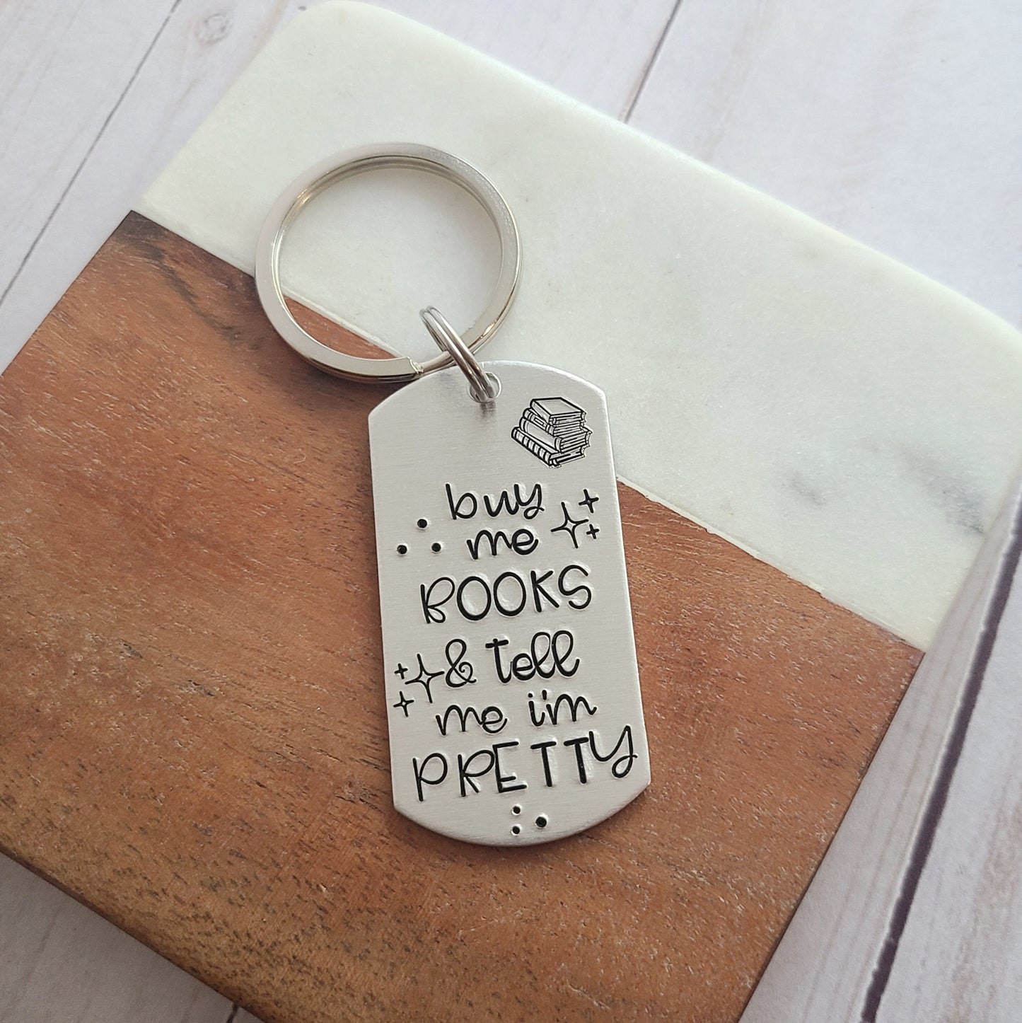 Silver dog tag shaped keychain that is hand stamped to read 'buy me books and tell me I'm pretty'