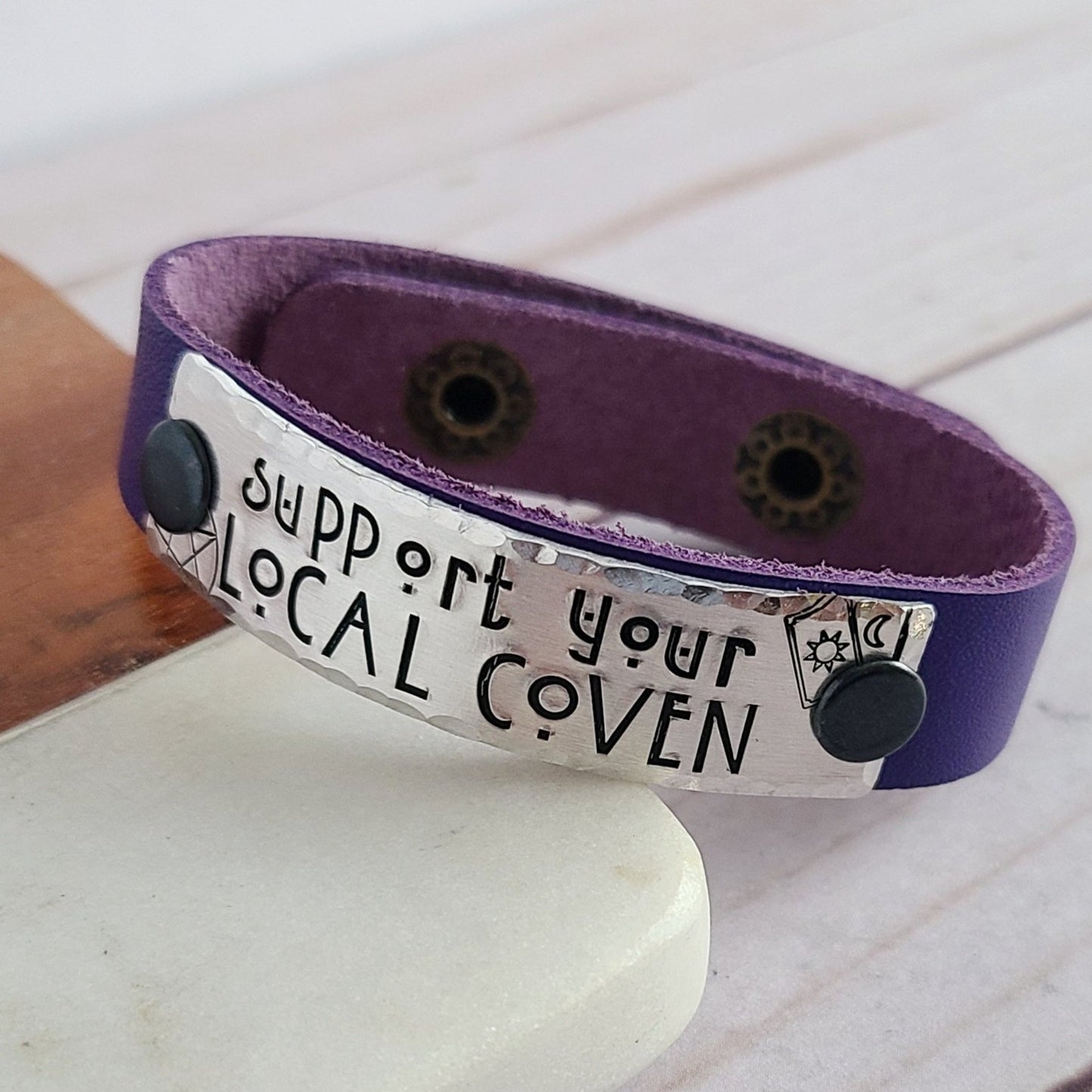 Purple leather cuff bracelet with a metal tag that is hand stamped with Support Your Local Coven