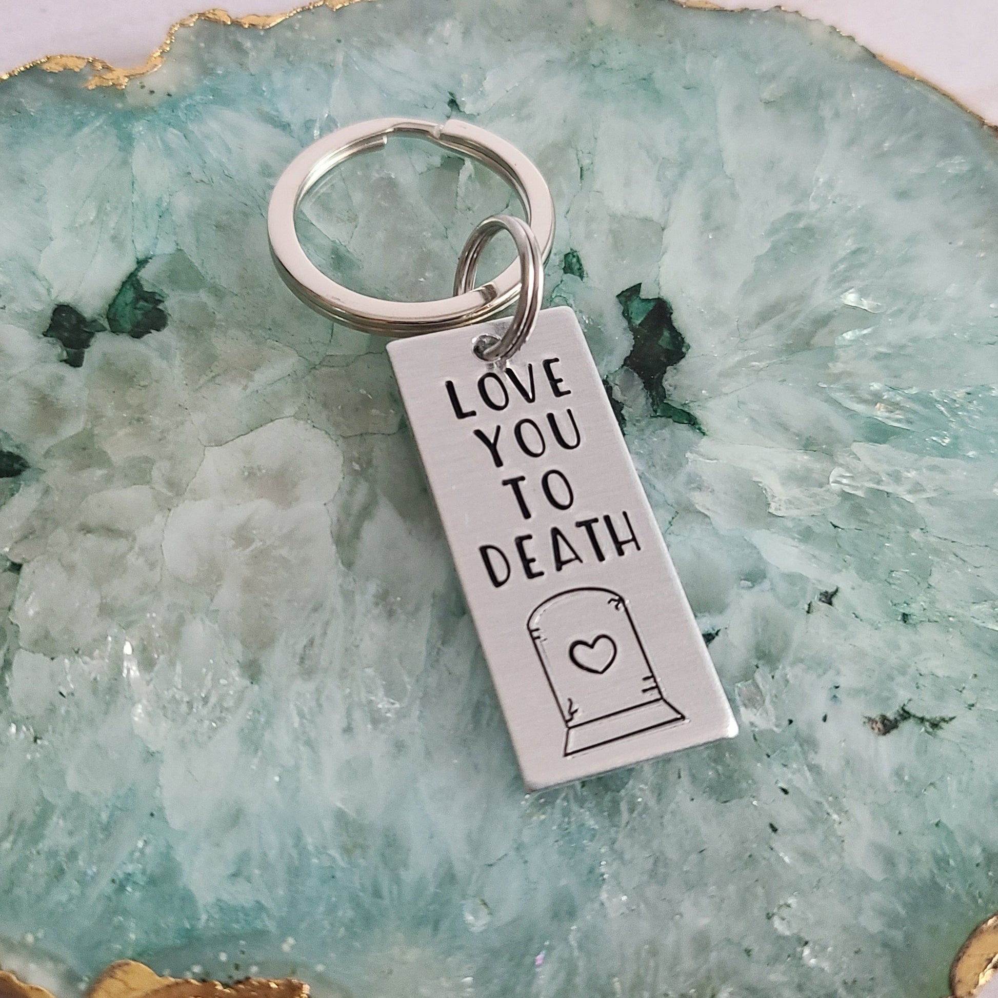 Silver Keychain that reads Love You To Death with the shape of a heart on a gravestone