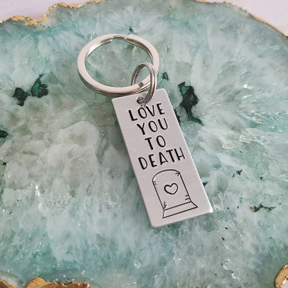 Silver Keychain that reads Love You To Death with the shape of a heart on a gravestone